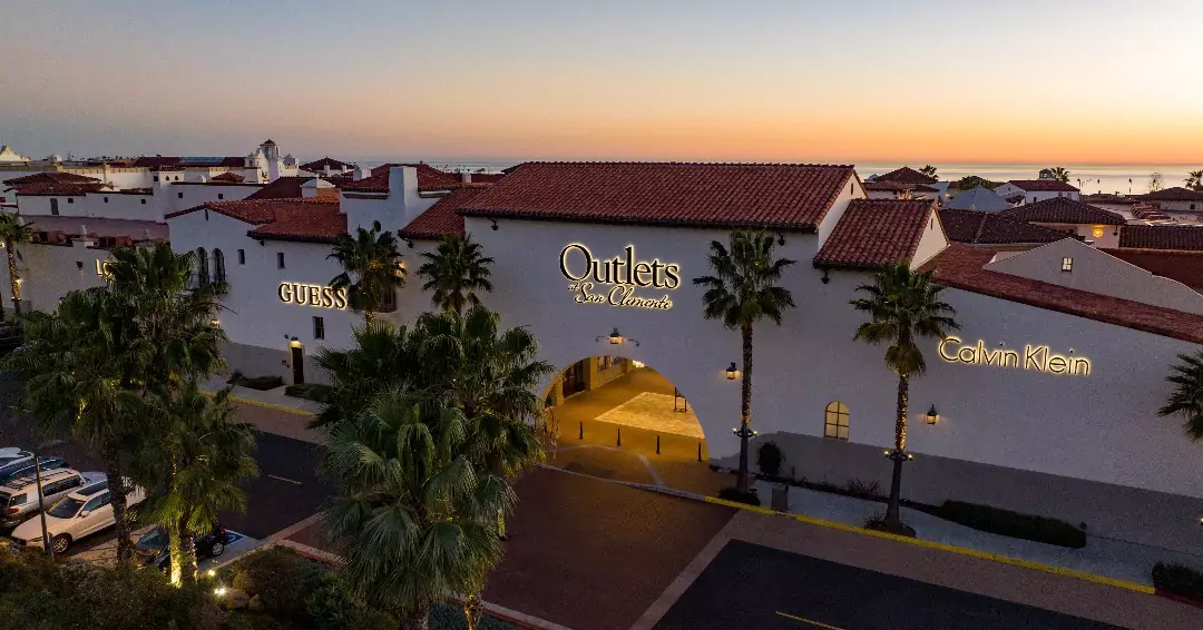 aerial view of the outlets at san clemente with a guess store and calvin klein at dusk with palm trees and parked cars in the foreground