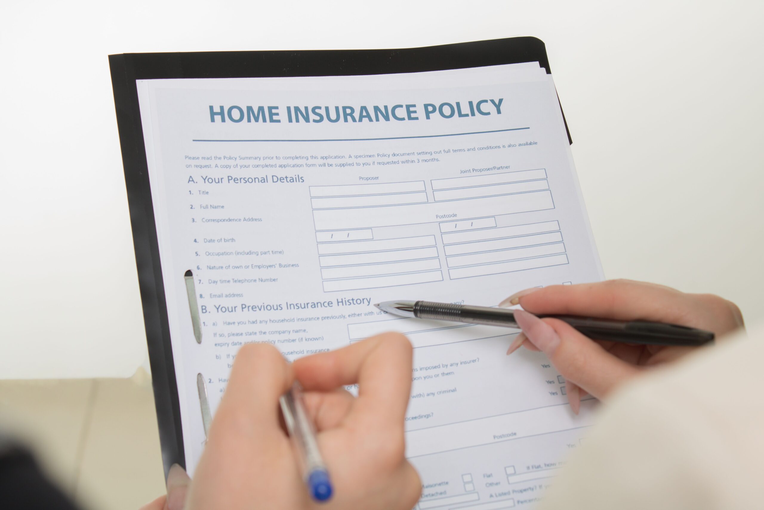 Hands holding pens filling out a home insurance policy document for coverage details on homeowners insurance in Orange County, California
